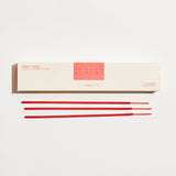 Red incense sticks in front of a white box with 'P.F. Candle Co' branding on a white background